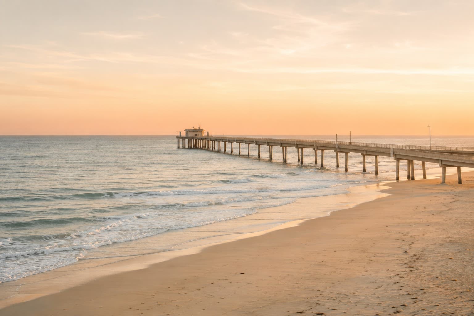 A wide Southern California beach with a long pier extending into the Pacific at golden hour